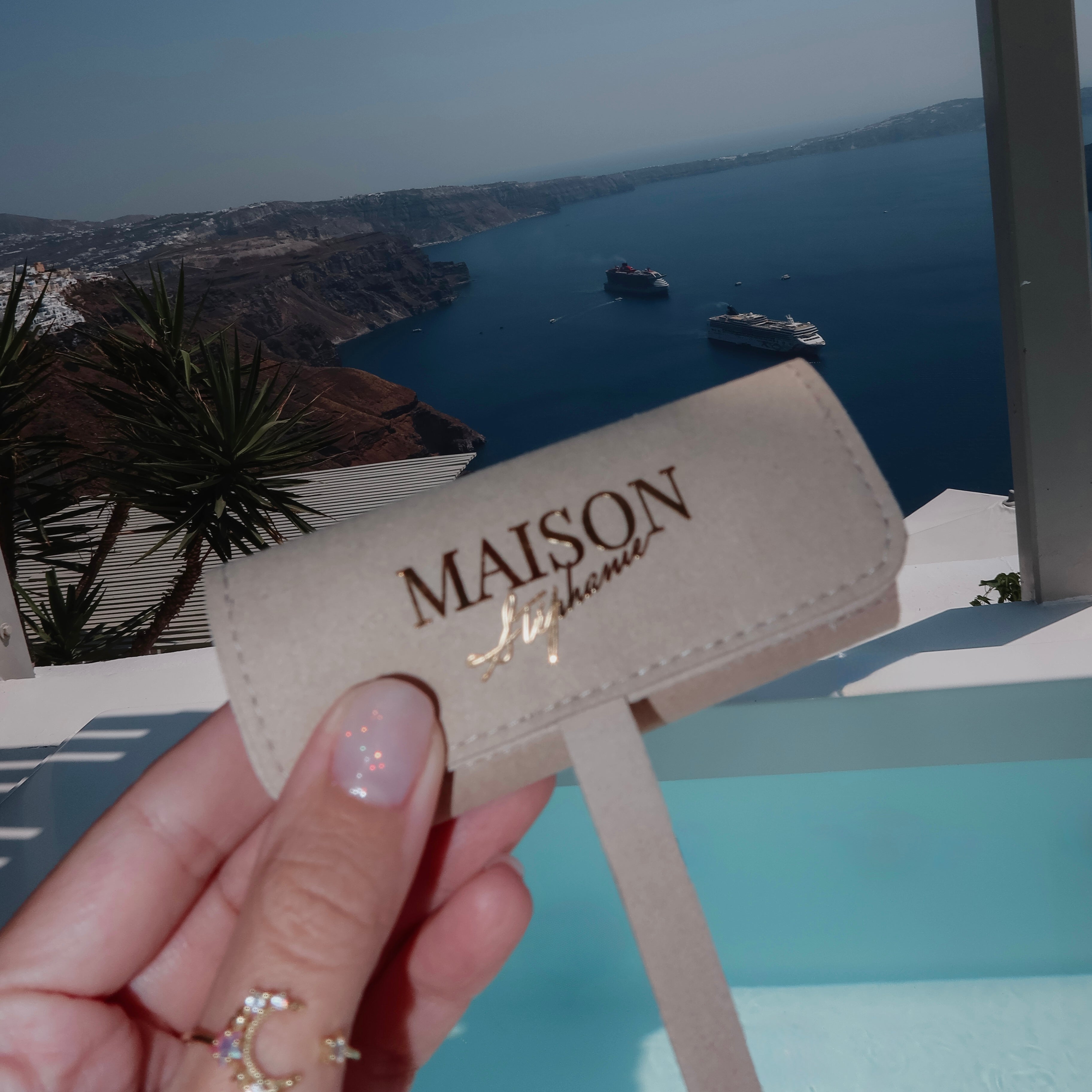 Travel Pouch MAISON Stéphanie Taupe pentru bijuterii, fotografiat în Santorini cu vedere spre caldera și Marea Egee, creat pentru organizarea accesoriilor în călătorii.