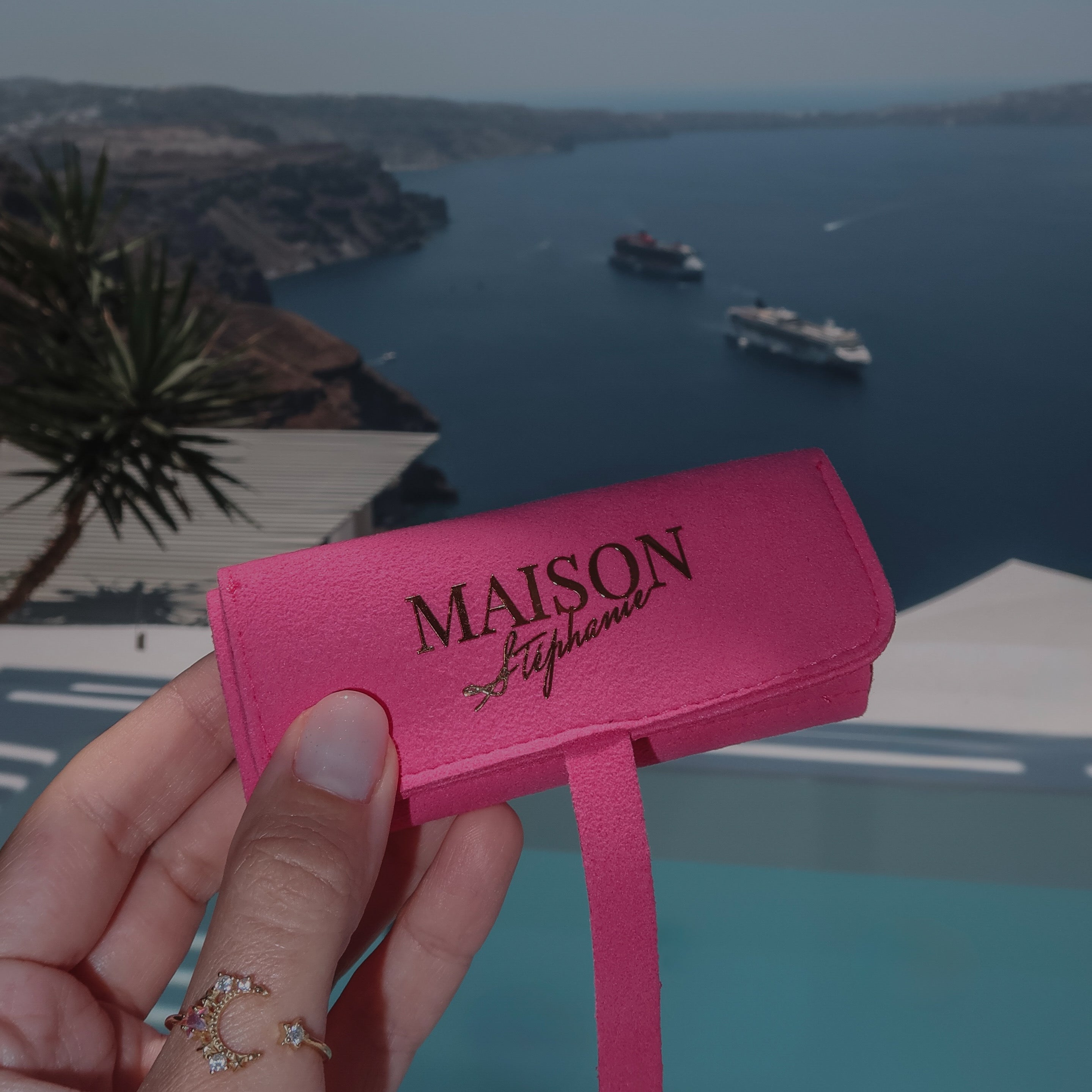 Travel Pouch MAISON Stéphanie Fuchsia pentru bijuterii, fotografiat în fața piscinei cu vedere spre caldera din Santorini, ideal pentru organizarea bijuteriilor în timpul călătoriilor.