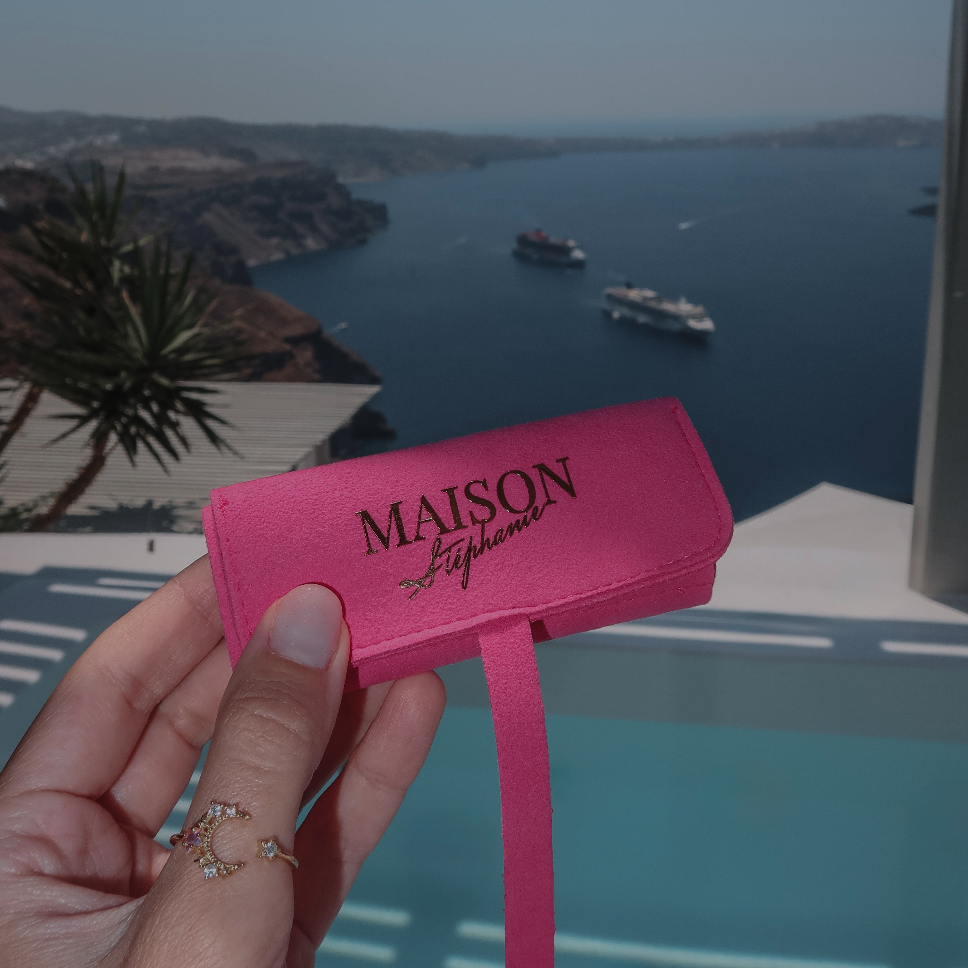 Travel Pouch MAISON Stéphanie Fuchsia pentru bijuterii, fotografiat în fața piscinei cu vedere spre caldera din Santorini, ideal pentru organizarea bijuteriilor în timpul călătoriilor.