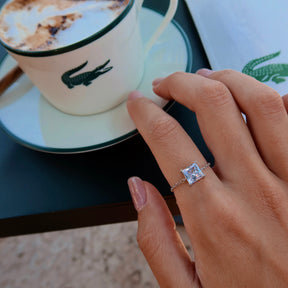 Inel cu piatră tăietură princess purtat pe mână lângă o ceașcă de cafea, fotografie lifestyle premium – MAISON Stéphanie.
